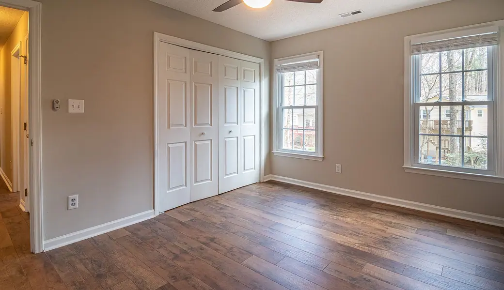 An empty bedroom with a hardwood floor and sunlight through the window