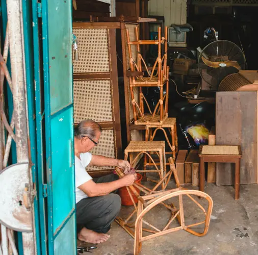 An older man repairing a rattan chair in his workshop